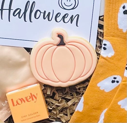 Pumpkin-shaped soap, 'Lovely' soap bar, and ghost-patterned socks on a Halloween-themed background.