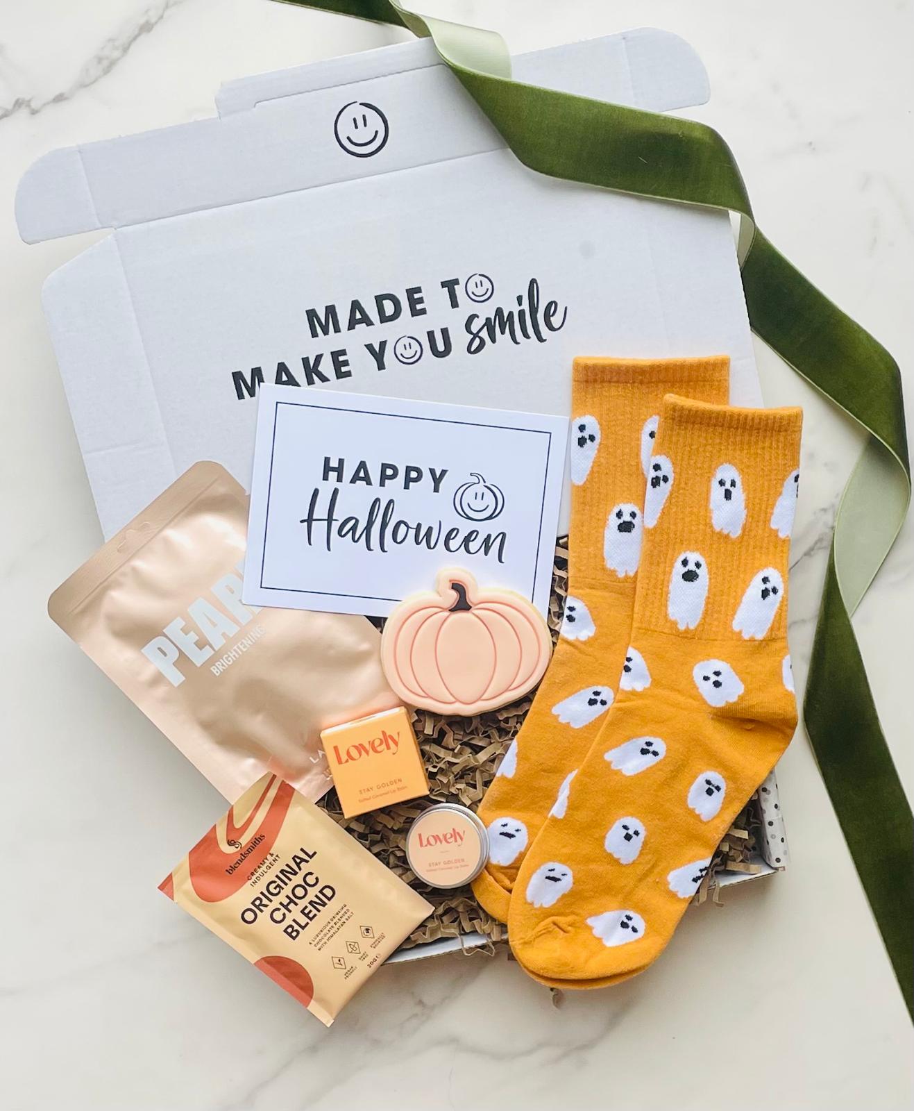 Halloween-themed gift set with socks, snacks, and a pumpkin decoration on a white background.