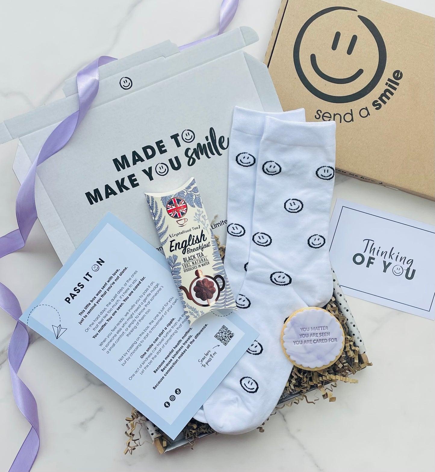 Gift set with socks, tea and card on a white surface with 'Send a Smile' branding