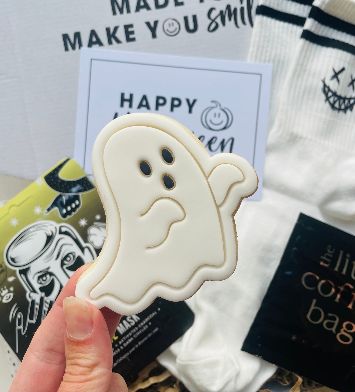 Hand holding a ghost-shaped cookie with Halloween-themed background