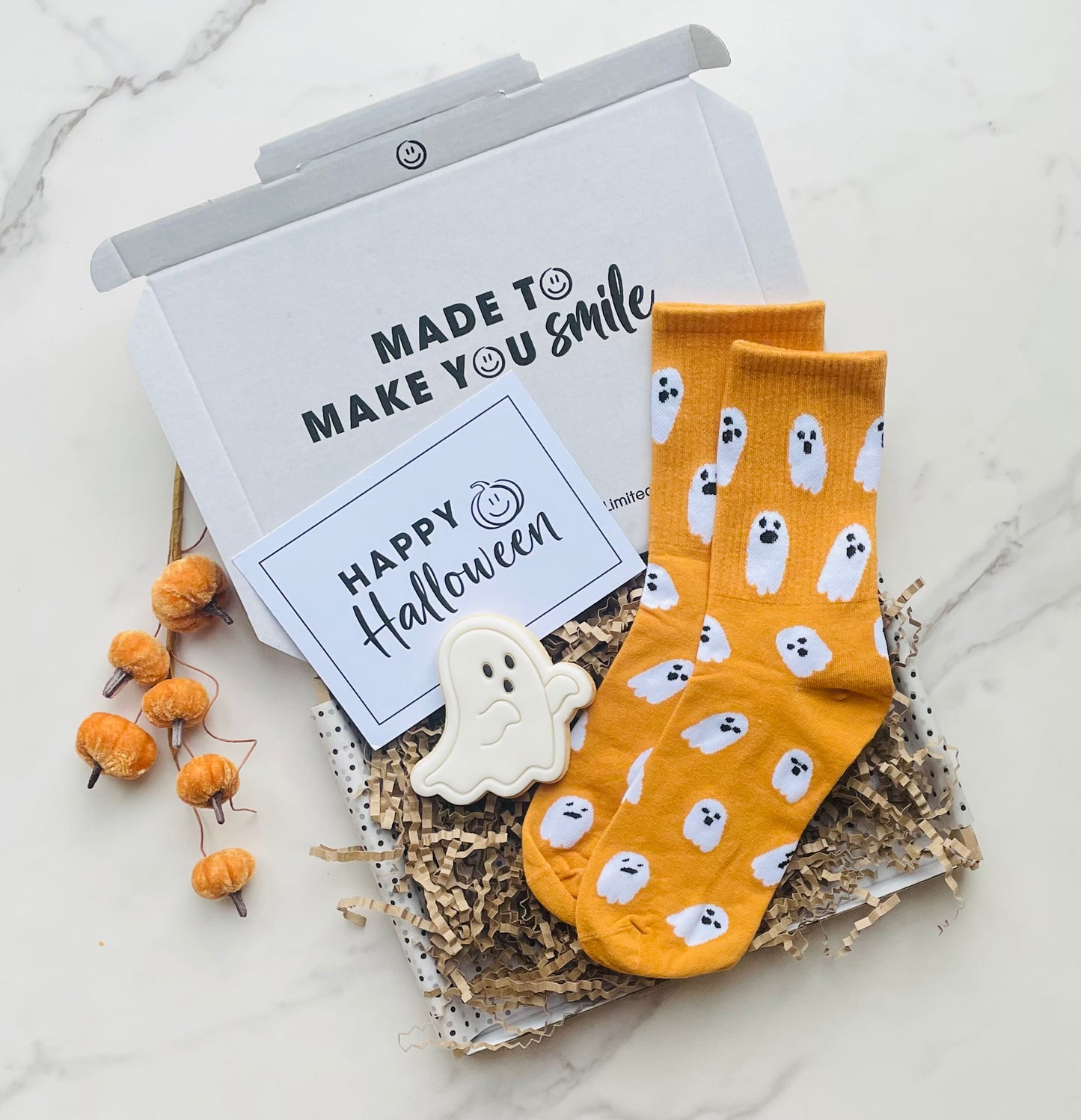 Pair of yellow socks with ghost patterns on a white surface with Halloween decorations.