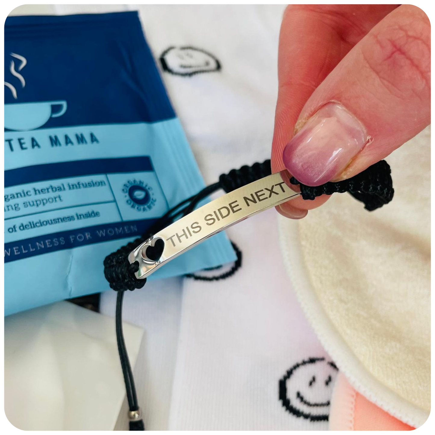 Bracelet with engraved message held by a hand, with 'Tea Mama' packaging in the background.