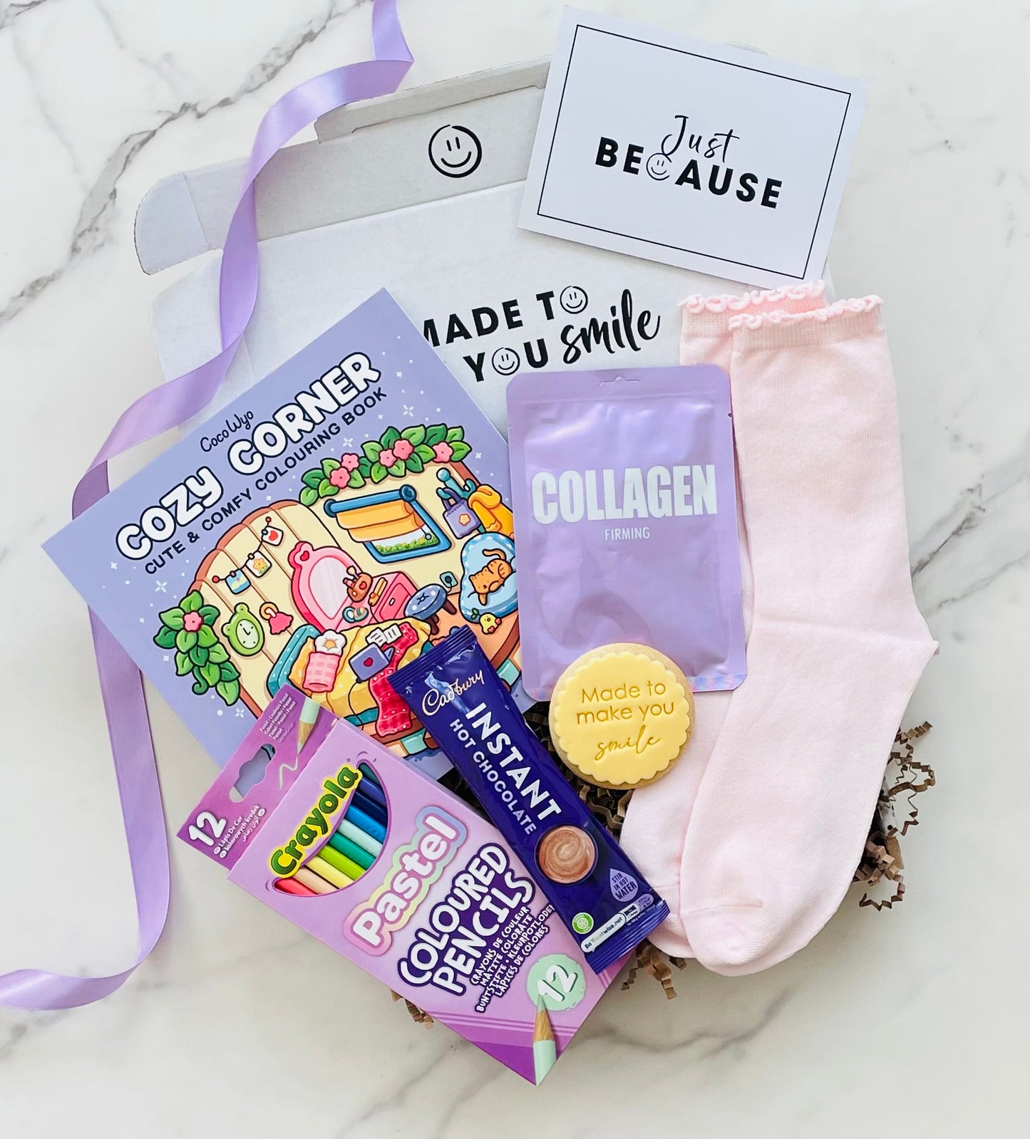 A gift box including a Coco Wyo Colouring Book, colouring pencils, sheet mask, hot chocolate sachet, made to make you smile cookie and pretty pink socks 
