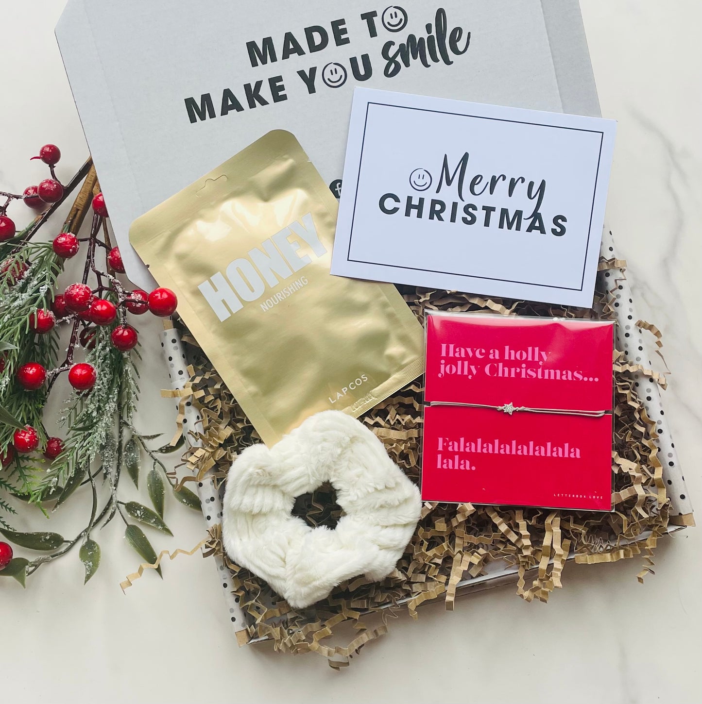 Christmas Letterbox Gift, including a Lapcos Sheet Mask, white fluffy hair scrunchie, Letterbox Love Bracelet 'Have a holly jolly Christmas' and a Merry Christmas Card. 