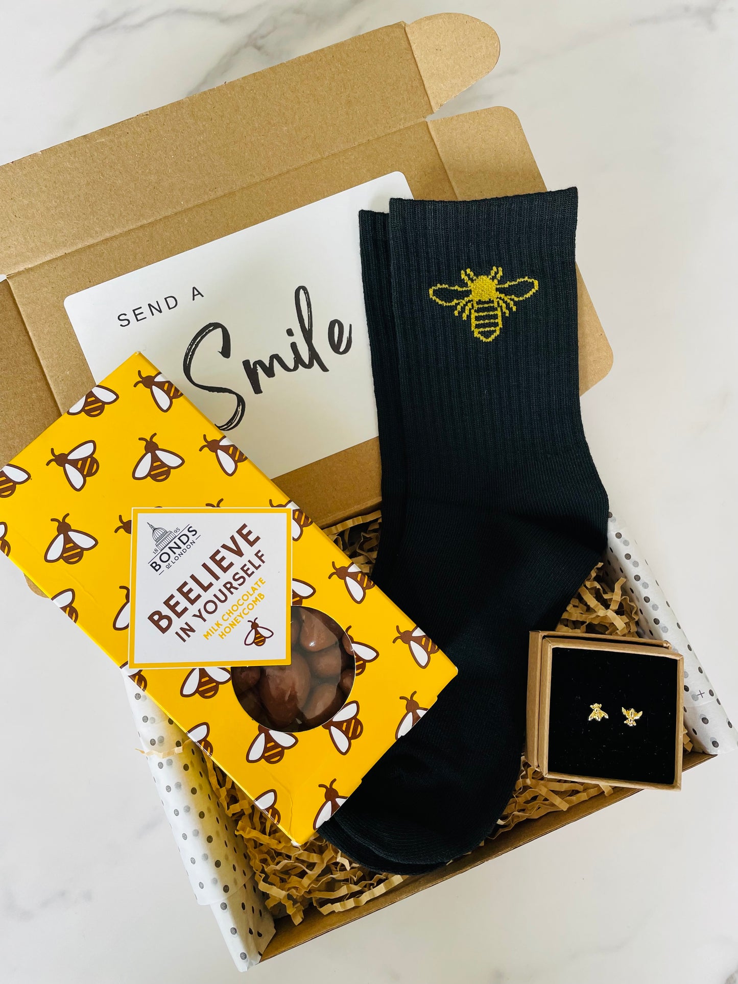 A gift box containing black socks with gold bee design, gold bee earrings and chocolate covered honeycomb. 
