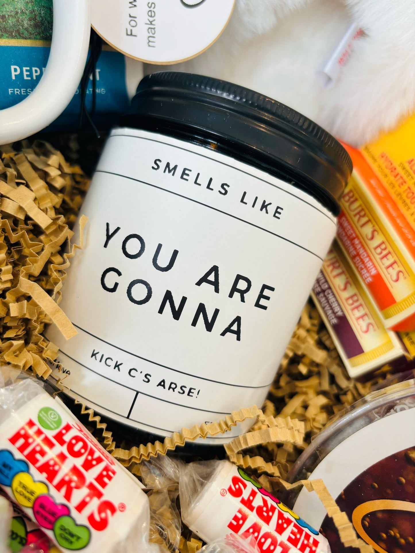 Jar candle with lid. White label with black wording Smells like you are gonna kick C's arse!