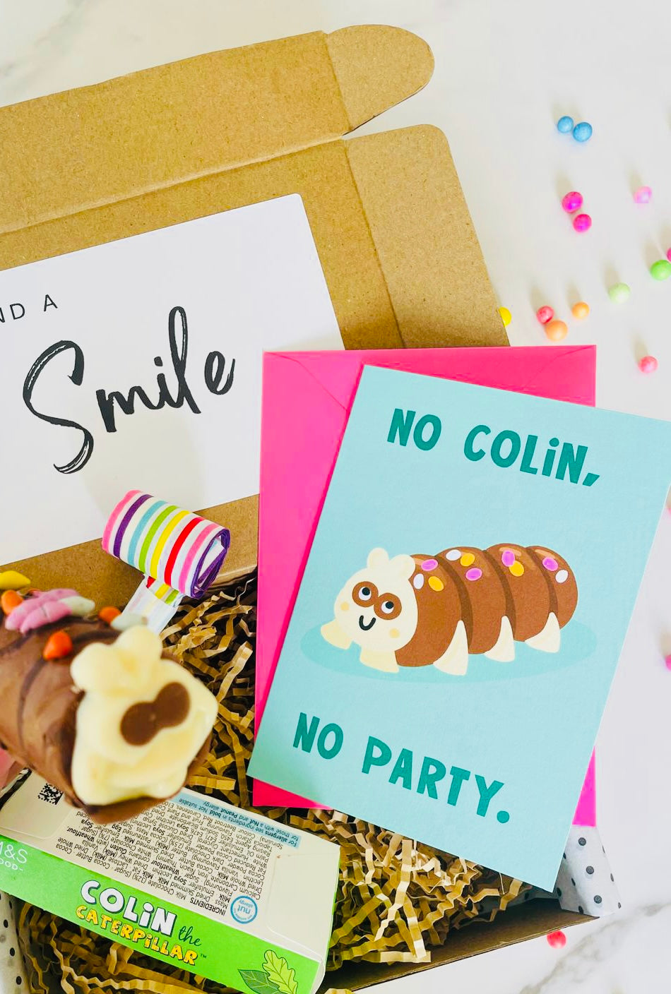  A vibrant Card displaying Colin the Caterpillar, No Colin, No Party, accompanied by a mini Colin the Caterpillar birthday cake and birthday blower inside a birthday gift box. 