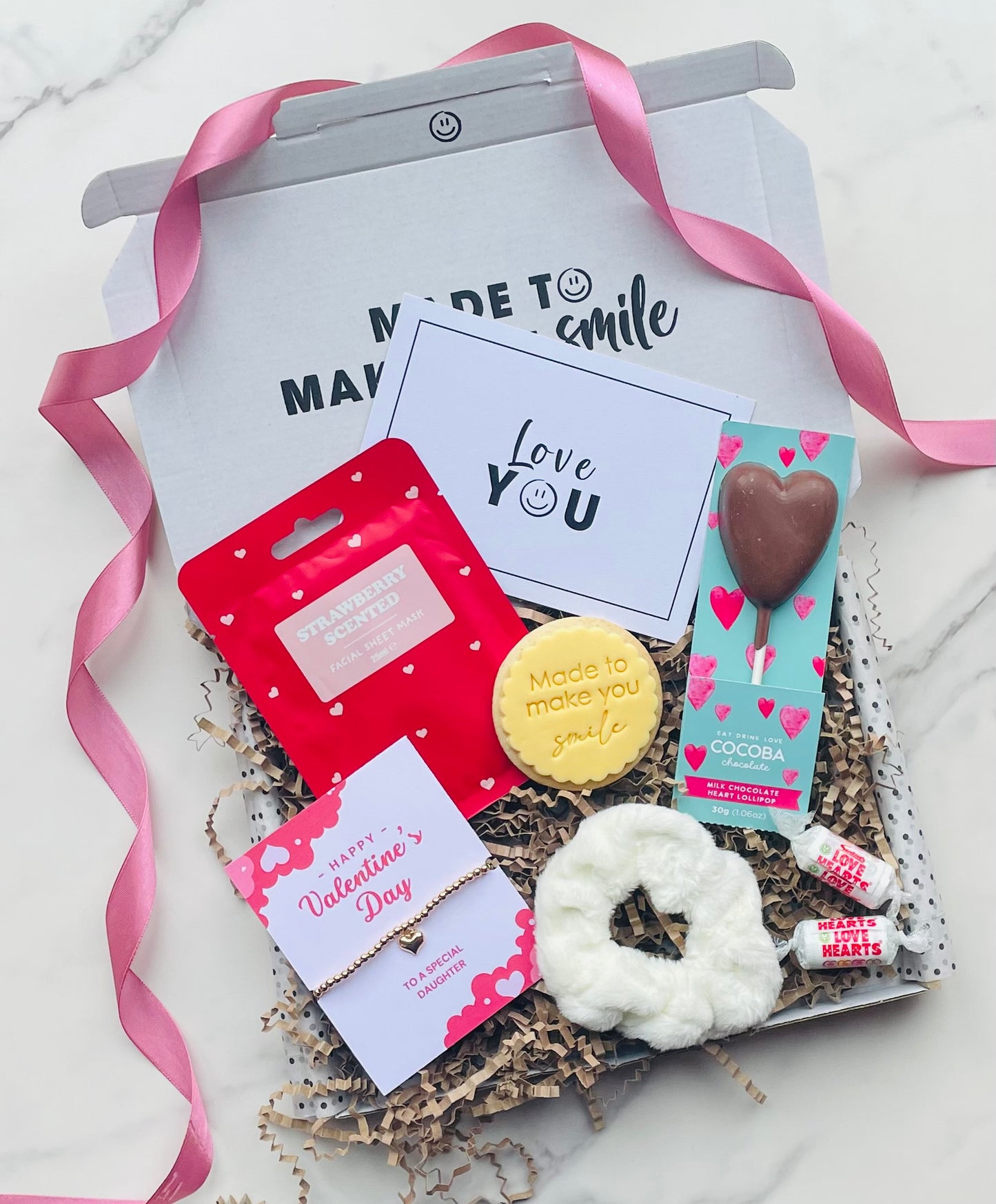 Valentines gift box for daughter, including, chocolate heart lollipop, strawberry scented face mask, gold hart bracelet, fluffy hair scrunchie, mini love hearts and a iced biscuit. 