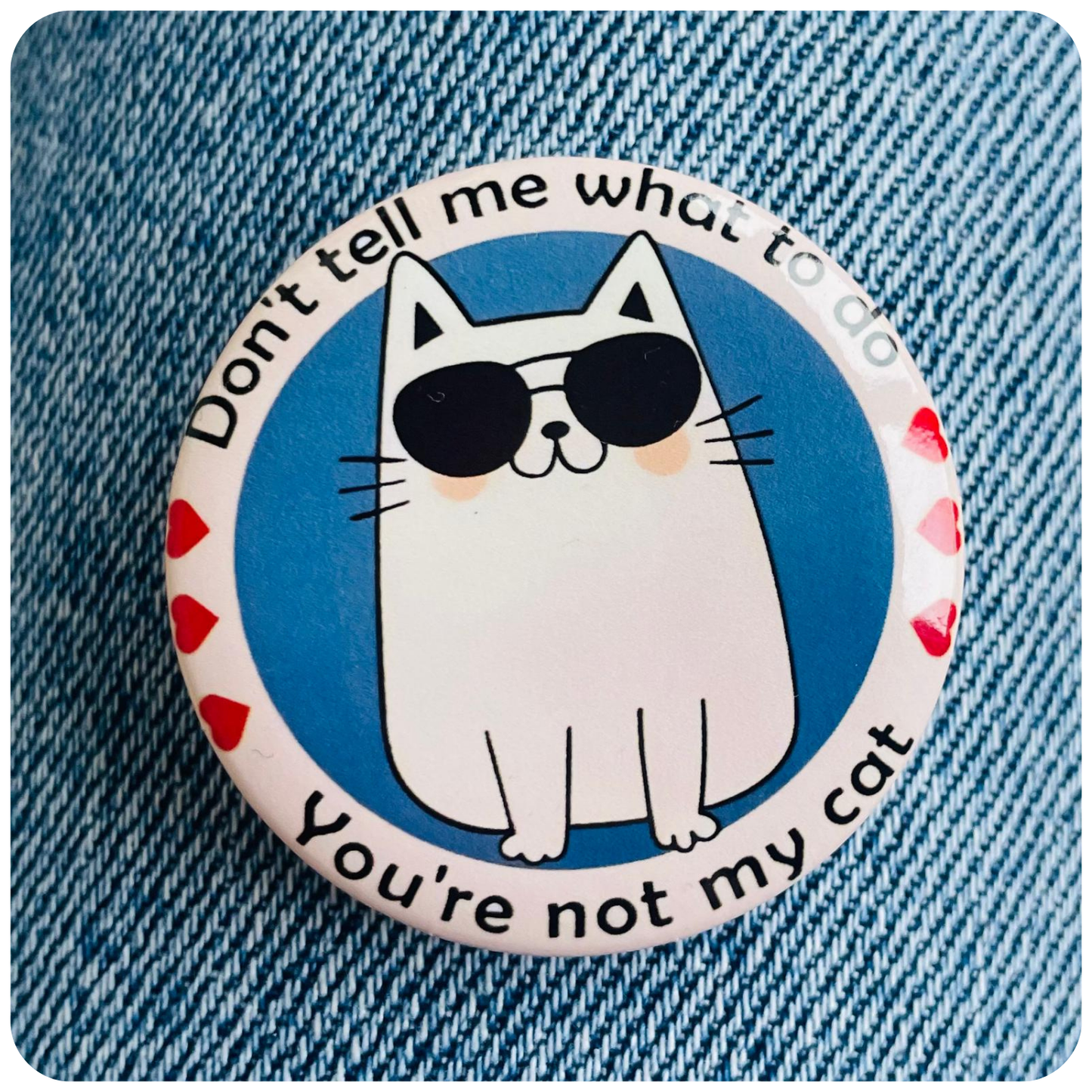 Button badge with a cat illustration and text on a denim background